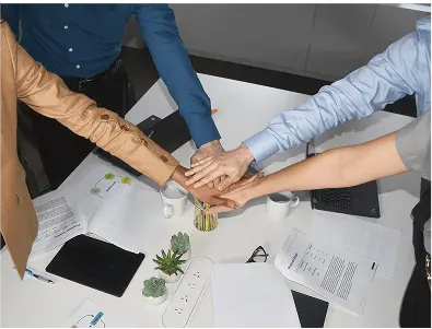 Team members placing their hands together over a meeting table with notes and documents