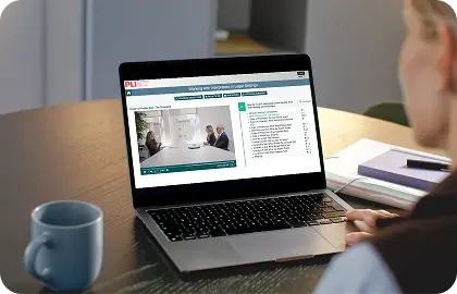Learner watching an online training video on a laptop and taking notes